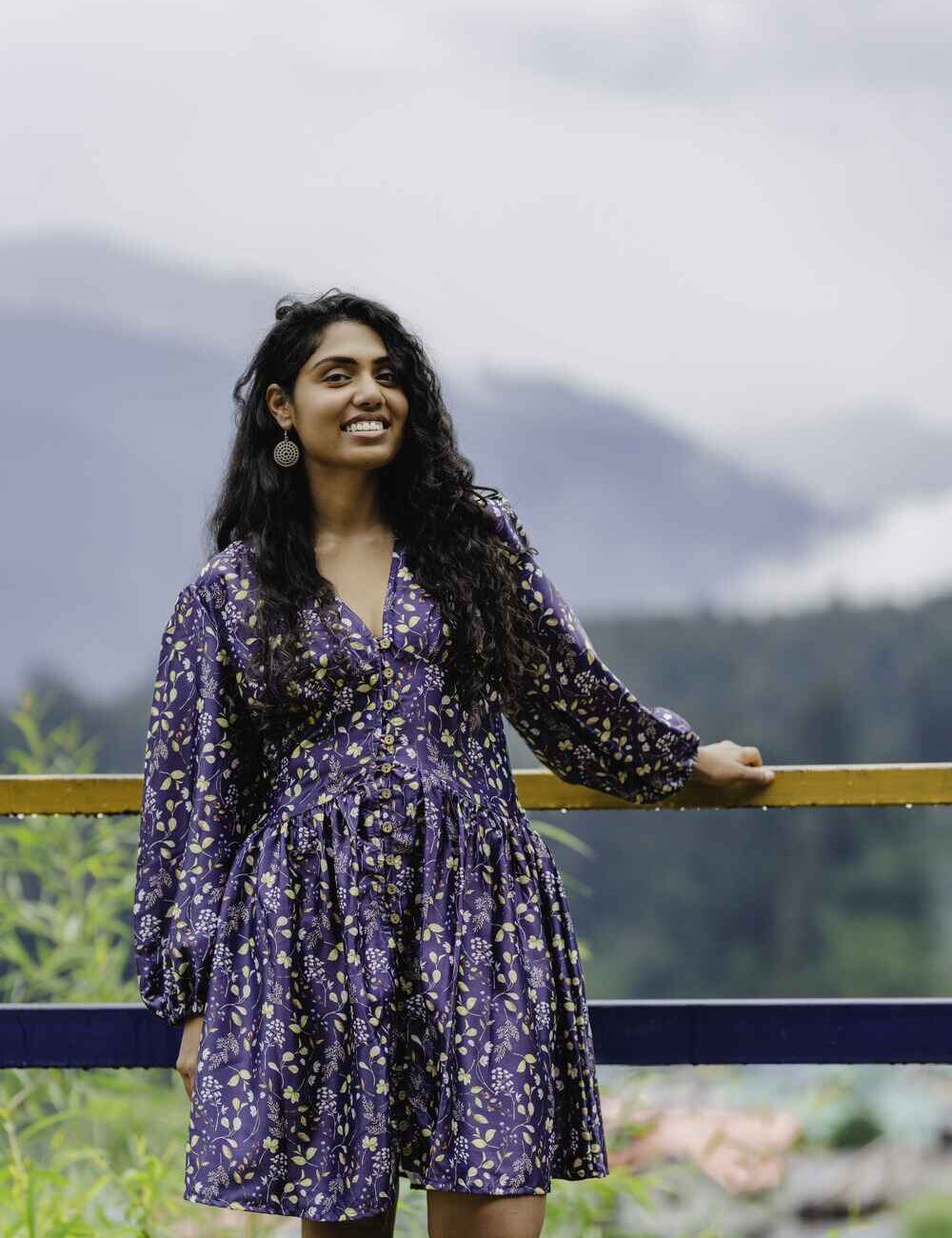 Model in a blue baby cotton floral short dress for women with long sleeves standing outdoors by a scenic mountain view.