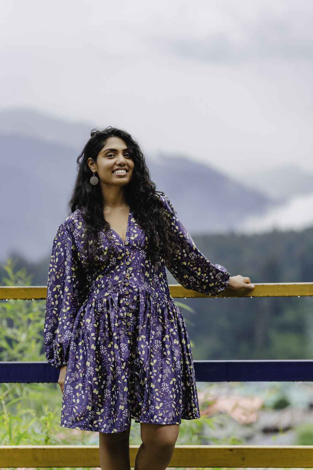 Model in a blue baby cotton floral short dress for women with long sleeves standing outdoors by a scenic mountain view.