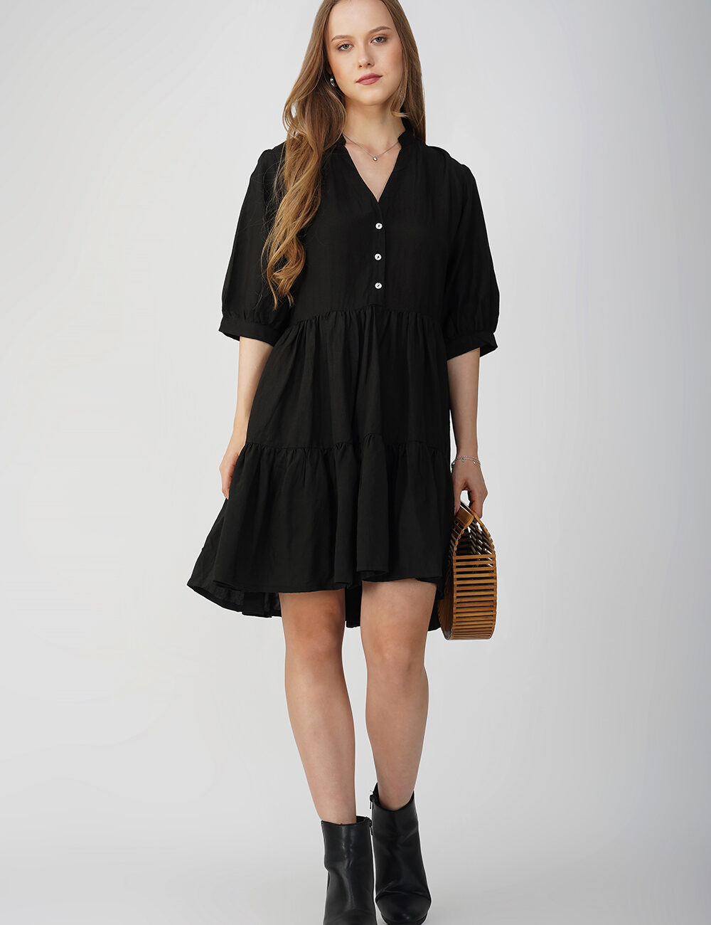 Model wearing a casual black cotton linen tiered dress with a relaxed fit and button-down detai